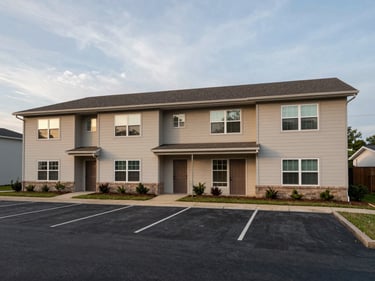 Wide exterior of a four-unit residential rental property in Springdale AR, two-story building, separate entry doors visible, overcast afternoon light, parking area in foreground, observed street-level framing
