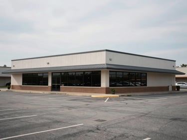 Wide exterior of a small commercial strip building in Bentonville AR, flat facade, parking lot in foreground, overcast midday light, real street-level perspective, no signage