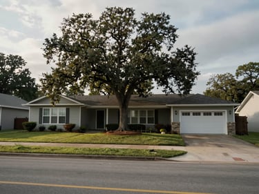 Wide exterior shot of a modest bungalow in Springdale AR on a flat street, morning light through overcast sky, mature oak in the front yard, observed framing showing the actual street context