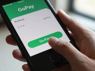Close-up of a thumb tapping a mobile payment screen showing a GoPay balance, indoors under natural window light, tight framing on the screen and hand
