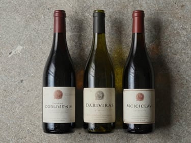 Overhead study of three wine bottles with aged labels arranged on a limestone surface, soft diffused light, no people, editorial still life