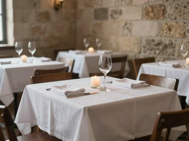 Empty restaurant dining room before service, white-linen table with wine glass and single candle, stone walls, northern natural light, no people