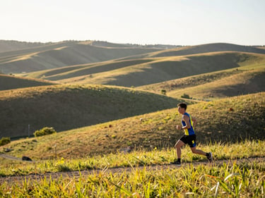Wide panoramic shot of the rolling foothills near Cochrane at sunrise, bright natural Alberta sunlight, vibrant athletic colors, shallow depth of field, 35mm