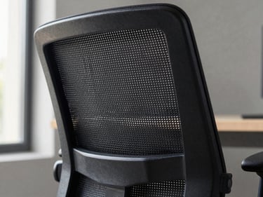 Close-up of an ergonomic executive office chair backrest, fine black mesh weave texture in sharp focus, aluminum armrest visible at the edge, soft natural window light from the left, neutral gray background, detail shot