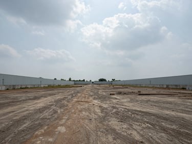 Wide ground-level shot of a cleared industrial plot at Savli GIDC, boundary walls visible, overcast daylight, open sky above, no people