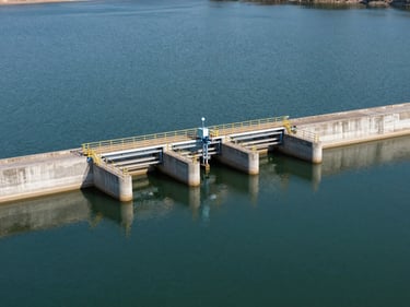 Wide environmental shot of a water treatment plant intake structure on a reservoir at critically low water level, daylight, concrete infrastructure visible above the waterline, no people