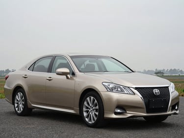 Front three-quarter driver-side profile of a champagne gold Toyota Crown, overcast daylight, full vehicle visible, squared frame