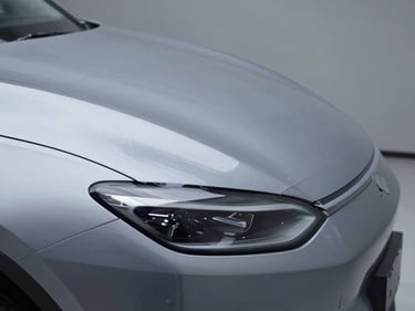 Extreme close-up of paint protection film applied to the leading edge of a vehicle hood, studio strobe lighting revealing the film's barely-there surface tension, cool neutral background, surgical framing emphasizing the precise film edge