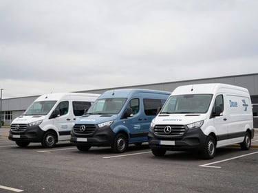 Three matching commercial vans in a clean urban parking bay, each wrapped in cohesive brand graphics, overcast daylight reading as neutral and controlled, low-angle 45-degree shot emphasizing the fleet's visual unity and three-dimensionality