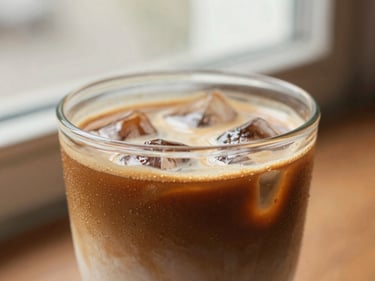Close-up of a perfectly layered iced latte in a clear glass, condensation on the outside. Warm natural light, shallow depth of field, rich coffee brown tones.