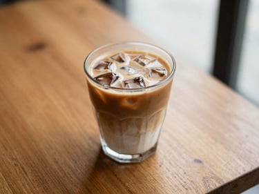 Overhead shot of an iced latte in a clear glass on a wooden table, warm light, shallow depth of field.
