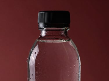 Macro close-up of a 330ml premium glass water bottle, clear glass, minimalist black cap, sharp studio reflections.