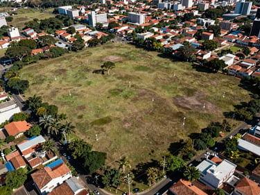 Overhead aerial-style shot of a flat land plot in a Brazilian urban fringe, clear boundary markers visible, surrounding neighborhood context, daylight