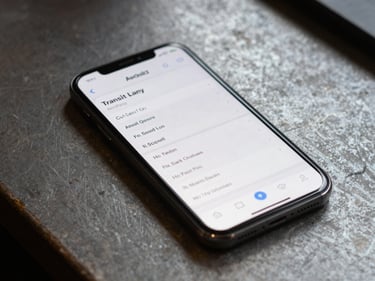 Android phone screen showing a transit scheduling app with high-contrast text, resting on a worn workbench surface, diffuse natural light from above, no hands visible