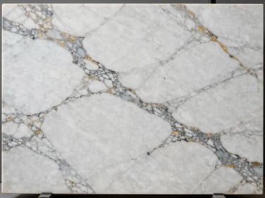 Overhead macro of polished Calacatta marble slab — bright white ground with bold grey and gold veining, controlled studio strobe, orthographic crop
