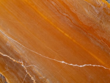 Overhead macro of polished Onyx Orange slab surface — translucent amber-orange tones with white vein lines, studio strobe lighting, tight orthographic framing