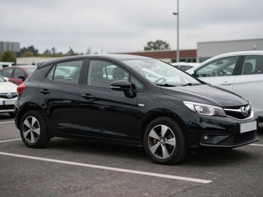 3/4-angle shot of a black compact hatchback parked on a dealer lot, overcast daylight, full vehicle visible from driver's side, neutral asphalt background