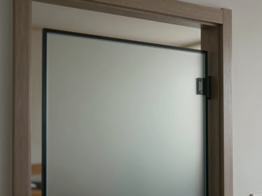 Detail shot of a smart glass panel mid-transition between opaque and clear states, visible in a residential interior doorway, soft even studio light, focus on the subtle gradient at the switching boundary