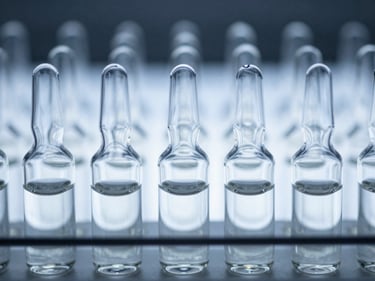 Close-up of sterile borosilicate glass vials arranged in a precise grid under cold blue-white light.