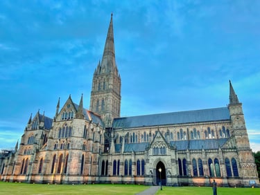 Historic Salisbury Cathedral featuring its iconic tall spire and Gothic architecture under a blue sky.