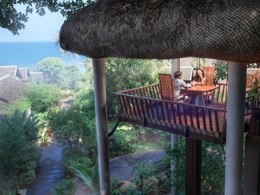 A couple having a romantic dinner in a treehouse-style balcony overlooking tropical greenery