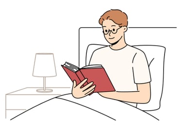 a man reading a book in bed with a lamp on the side