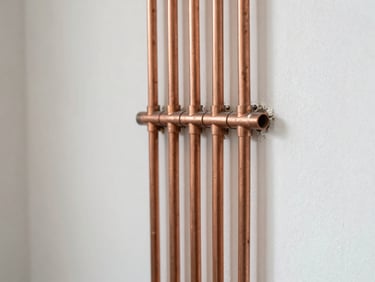 Detail of copper heating pipes neatly installed on a clean white utility wall, soft natural side light, 35mm editorial photography
