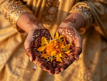 Close-up of hands adorned with intricate henna patterns holding marigold petals during a traditional ceremony, warm golden-hour light, shallow depth of field
