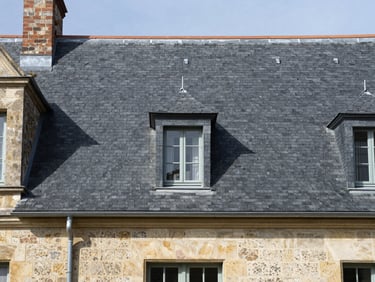 Crisp architectural photography of a restored slate roof on a historic French stone house, perfectly aligned natural slates, zinc gutters, bright daylight, 35mm lens