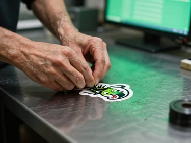 Close-up of a technician weeding a custom vinyl sticker on a dark metal workbench, moody green ambient reflection from a nearby screen, high contrast.