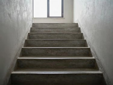 Eye-level view down a freshly mopped staircase in a residential building, natural light from a landing window, clean concrete steps