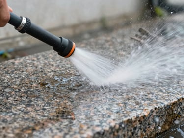 Close-up macro shot of a high-pressure water jet cleaning a rough granite paving stone, water and debris spraying to the side, natural overcast daylight, stone texture clearly visible