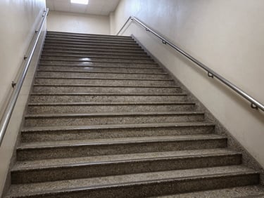 Wide shot of a spotless commercial stairwell, freshly mopped stone steps, handrail wiped clean, neutral artificial light from above — no people, honest documentation