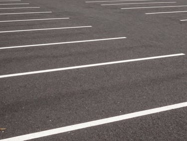 Wide environmental shot of a freshly striped commercial parking lot with crisp white lines under bright midday sun, 35mm