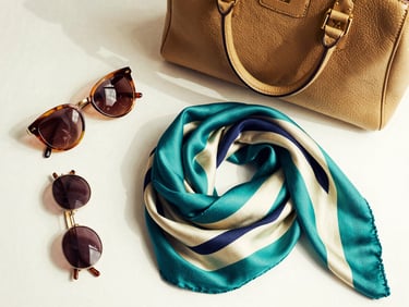 Flat lay of luxury brand accessories, elegant handbag, sunglasses, and a silk scarf, high-contrast, soft studio lighting, rich gold tones, medium format film.