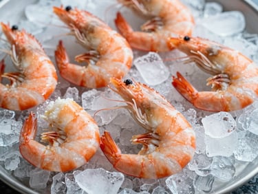 Camarones enteros glaseados sobre hielo picado, en una bandeja de acero inoxidable, con luz fría y detalles de textura.