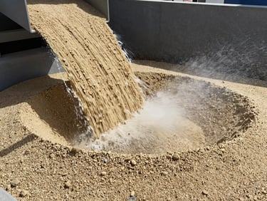 Close-up of clean, washed manufactured sand cascading through an industrial wet classifier, water spraying, high-contrast natural daylight, gritty texture