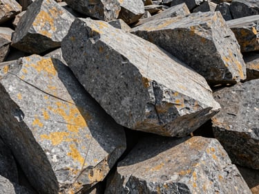 Huge raw granite boulders stacked in quarry, sharp angular fractures, dramatic natural lighting