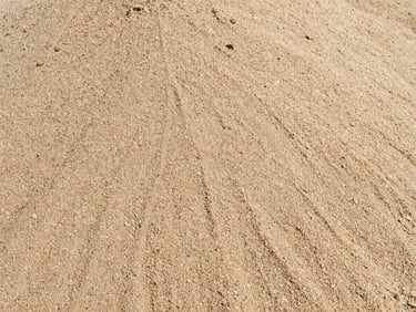 Close-up of dry, perfectly graded manufactured sand, fine grain texture, high-contrast daylight