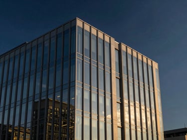 Crisp architectural twilight photography of a modern glass office building exterior, clean geometric lines, deep navy sky, sharp reflections