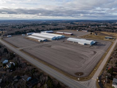 Wide-angle drone shot of a flat, cleared 50-acre industrial plot in Cape Breton, bounded by a major highway, overcast morning light.