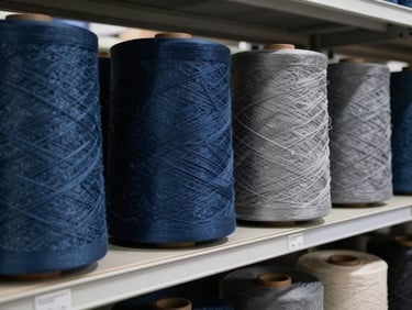 Rolls of high-quality raw textiles in deep blue and grey shades stacked on shelves in a modern clean warehouse