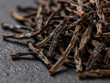 Macro close-up of premium loose-leaf Ceylon black tea leaves on a dark textured surface, warm side lighting highlighting the rich textures