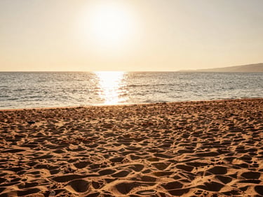 Editorial photography, wide sandy beach in Gela Sicily, low golden-hour sun reflecting on calm Mediterranean sea, terracotta-toned sand, high-end travel aesthetic