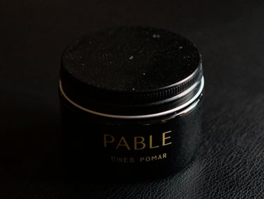 Close-up of an elegant, minimalist black pomade jar with gold lettering, sharp focus, low-key dramatic lighting, on a dark leather surface, 35mm film