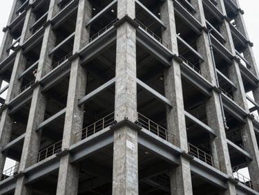 High-contrast structural view of a commercial tower featuring heavy steel framing and raw concrete pillars.