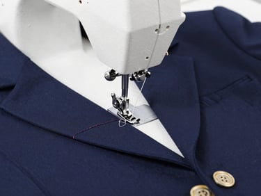 Close-up of industrial sewing machine stitching a reinforced seam on a navy school uniform blazer, bright studio lighting, sharp focus on needle and thread.