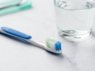 Close-up of modern dental hygiene tools, a clean toothbrush, and a glass of water on a white marble surface, soft green and blue accents, bright natural light, 35mm
