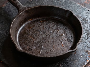 Heavy cast iron skillet with raw iron texture on a dark industrial metal sheet, overhead shot