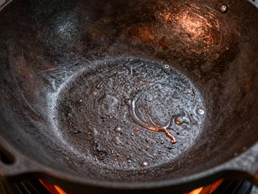 Macro photography of the textured surface of an uncoated cast iron wok, highlighting the raw iron grain and warm copper accents.